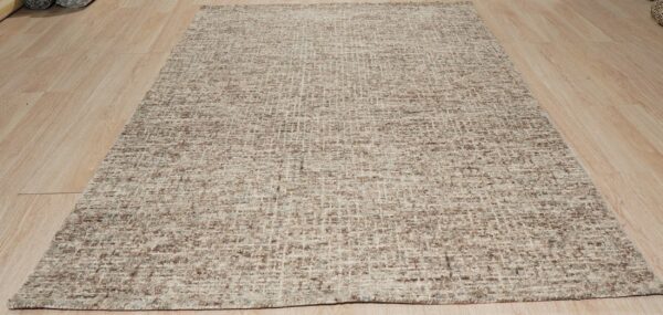 Chunky woven rug featuring an irregular beige and brown grid pattern displayed on light wood flooring.