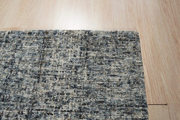A highly textured blue and gray mottled rug with chunky loops lies on light wooden flooring.