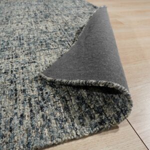 Chunky, textured blue and gray rug lifted to show its dark gray backing on light wood flooring.