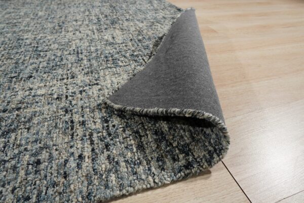 Chunky, textured blue and gray rug lifted to show its dark gray backing on light wood flooring.