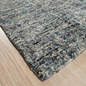 A corner of a chunky textured rug showing mixed blue, gray, and cream colors on light hardwood.