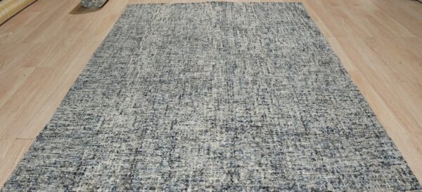Gray speckled rug with low pile texture displayed on blonde hardwood planks.