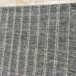 Textured gray rug featuring white and tan vertical columns lying on light plank flooring.
