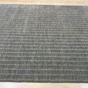 A dark gray textured rug with thin white horizontal stripe detailing rests on light wood plank flooring.