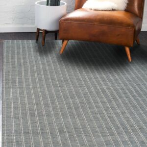 Low pile blue rug with thin vertical stripes next to a brown leather armchair and white brick wall.