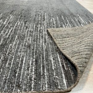 Textured gray rug with irregular white stripes, folded over to show the tightly woven backing on light wood flooring.
