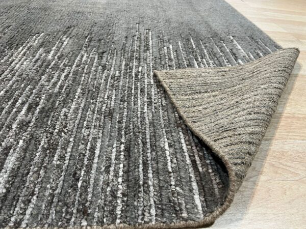 Textured gray rug with irregular white stripes, folded over to show the tightly woven backing on light wood flooring.