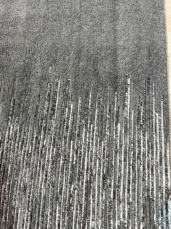 Textured dark gray rug featuring fading vertical white and black textured cords on wood flooring.