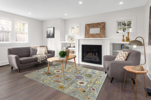 A distressed blue and gold floral rug defines a bright living room space with dark hardwood floors.