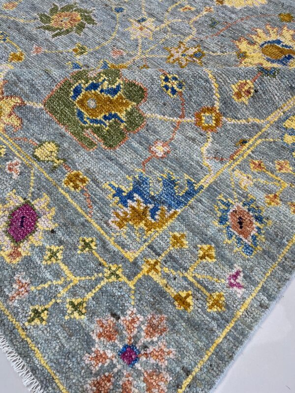 Close-up of a heathered blue-gray rug featuring traditional floral patterns in yellow, green, blue, and magenta.