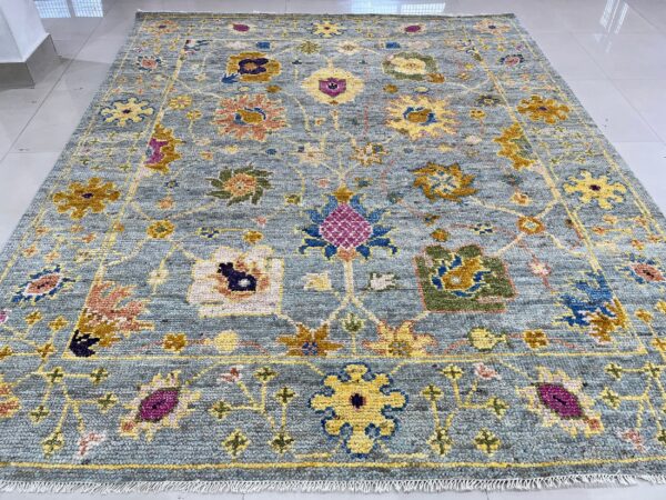Dusty blue rug with yellow, magenta, and green floral patterns lying on light gray tiles.