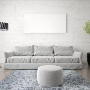 A blue and gray block patterned rug anchors a light grey sofa and ottoman on wood floors.