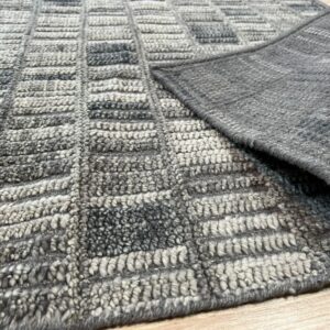 The high-pile, nubby gray and light gray geometric rug corner is folded back on light wood flooring.