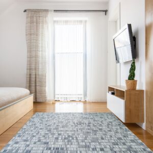 A blue, gray, and white abstract rug on a wood floor in a brightly lit modern bedroom.