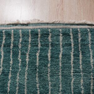 Close-up of a teal and cream high-pile rug with vertical stripes, lying on light wood flooring.