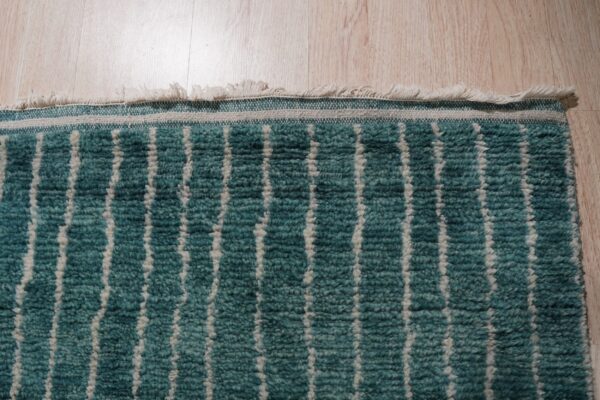 Close-up of a teal and cream high-pile rug with vertical stripes, lying on light wood flooring.