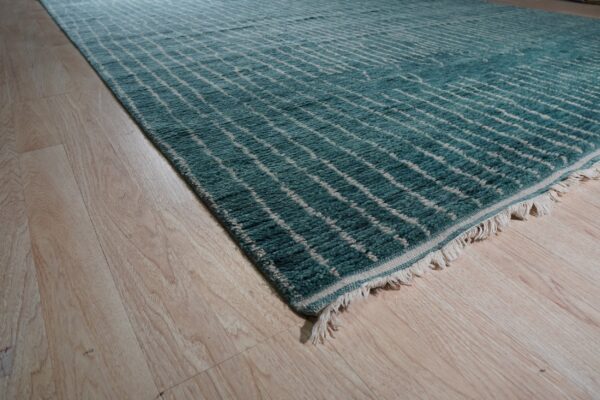 High-pile teal rug with an off-white geometric grid and visible fringe rests on light wood plank flooring.