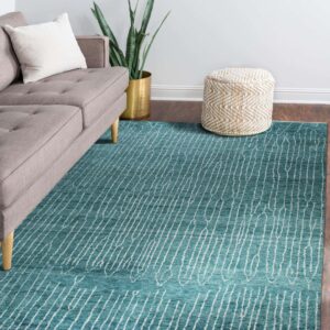 A turquoise rug with white abstract striping sits beneath a gray sofa on dark wood flooring.