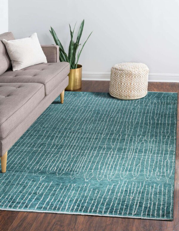 A turquoise rug with white abstract striping sits beneath a gray sofa on dark wood flooring.