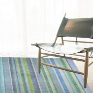 Multi-colored striped rug in blues, greens, and gray accents under a modern wood and dark leather chair.
