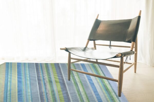Multi-colored striped rug in blues, greens, and gray accents under a modern wood and dark leather chair.