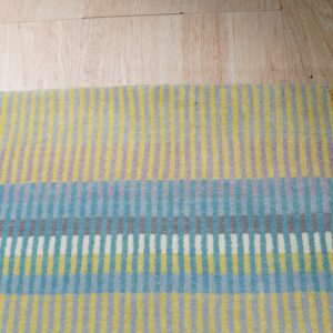Multi-colored low pile rug with varied vertical stripes rests on light blonde wood flooring.