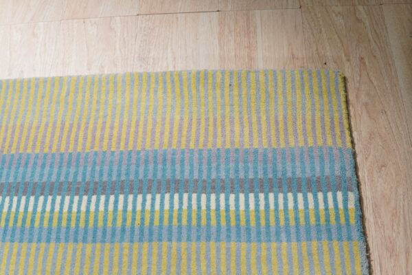 Multi-colored low pile rug with varied vertical stripes rests on light blonde wood flooring.