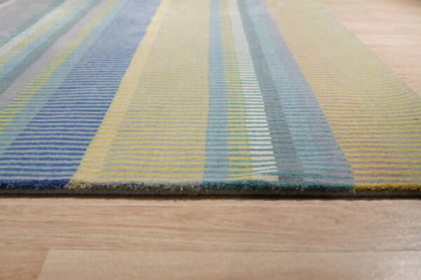 Low-pile rug with blue, yellow, and gray vertical stripes lying on light wood flooring.