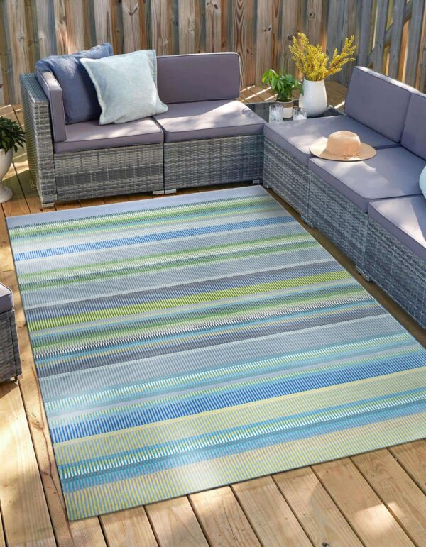 Multicolored striped outdoor rug anchors a gray woven sectional on a sunlit wooden deck.
