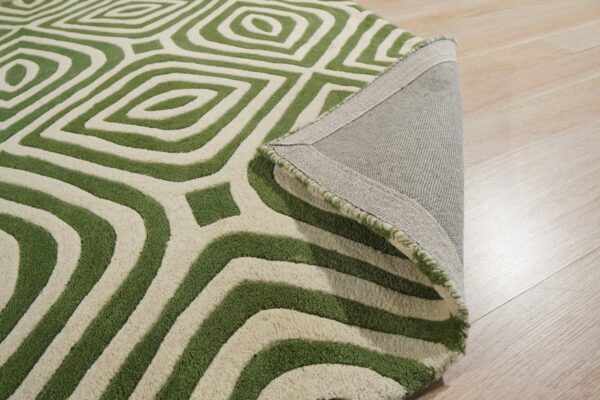 Textured green and cream rug with a geometric pattern, partially folded on light wood flooring.