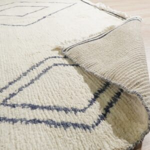 The textured cream rug with blue geometric lines is rolled back, showing the flat woven backing.