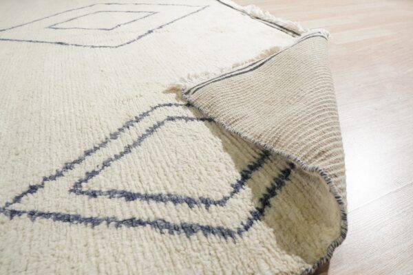 The textured cream rug with blue geometric lines is rolled back, showing the flat woven backing.