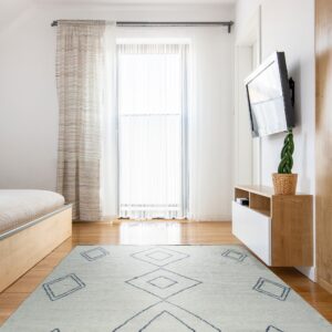A pale rug with dark blue diamonds covers wood flooring near a bed and floating media console.