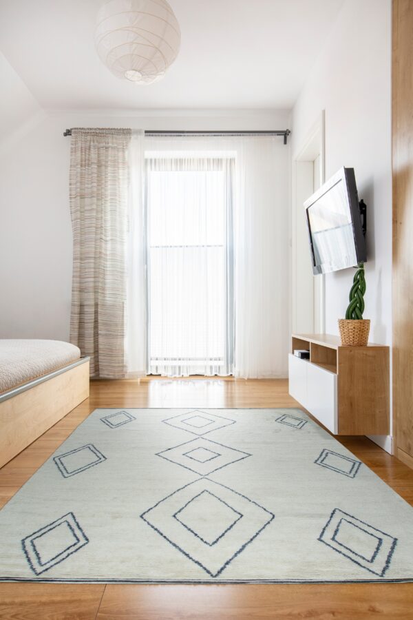 A pale rug with dark blue diamonds covers wood flooring near a bed and floating media console.