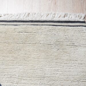 High-pile cream rug with dark angular patterns, black stripes, and fringe lies on light wood flooring.