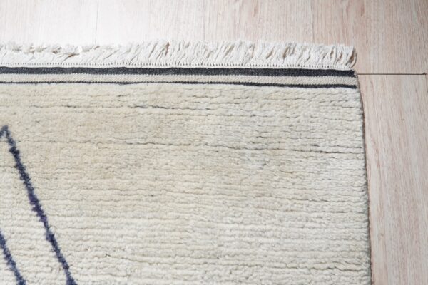 High-pile cream rug with dark angular patterns, black stripes, and fringe lies on light wood flooring.