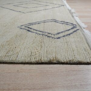 Textured off-white rug with dark blue geometric diamond motifs and fringe on pale wood floors.