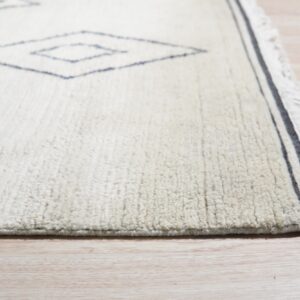 High-pile ivory rug with sparse navy geometric diamonds and striped fringe border on light flooring.