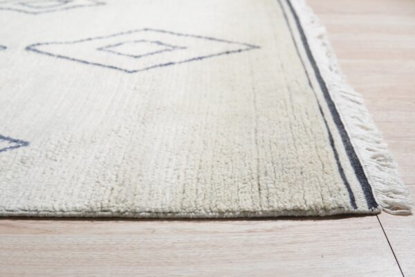 High-pile ivory rug with sparse navy geometric diamonds and striped fringe border on light flooring.