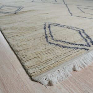 Close-up of a shaggy ivory rug with dark geometric diamonds and white fringe on light wood flooring.