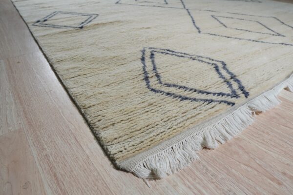 Close-up of a shaggy ivory rug with dark geometric diamonds and white fringe on light wood flooring.