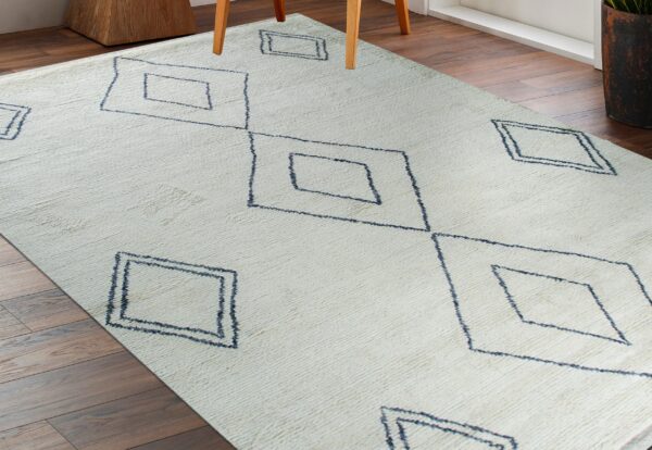 Cream textured rug with dark blue geometric diamond patterns on a dark wood floor.
