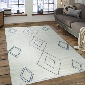 A cream textured rug featuring navy diamond outlines rests on distressed wood floor planks near a gray sofa.