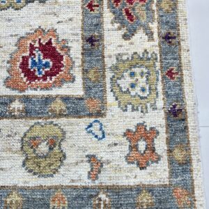 Textured close-up of a rug corner with a cream field, gray border, and motifs in red, yellow, and blue.