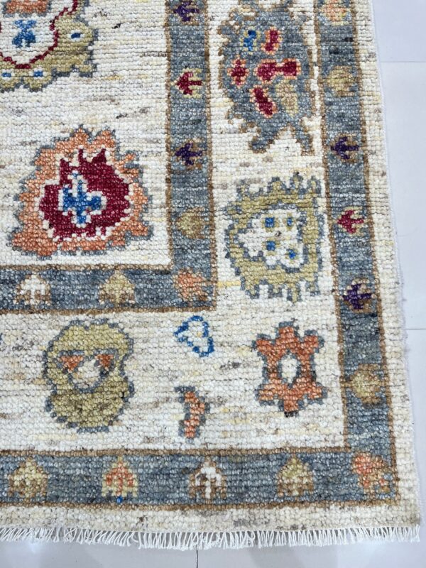Textured close-up of a rug corner with a cream field, gray border, and motifs in red, yellow, and blue.