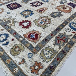 High-pile area rug featuring colorful geometric patterns on a cream field and a thick grey border on tile flooring.