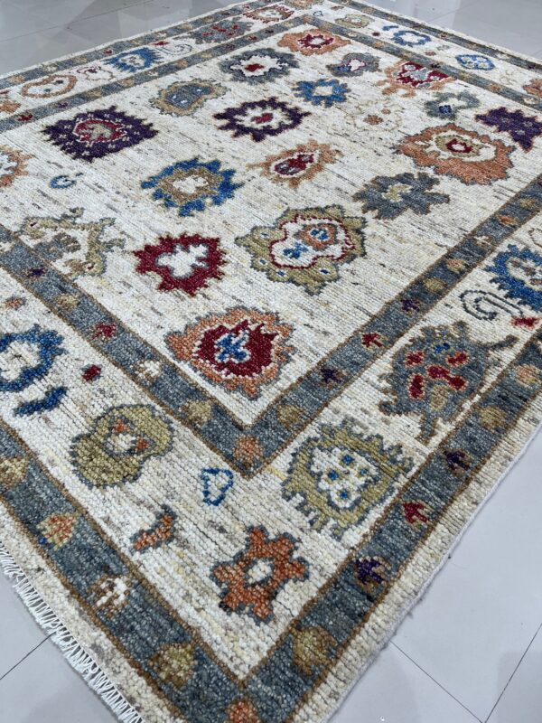 High-pile area rug featuring colorful geometric patterns on a cream field and a thick grey border on tile flooring.