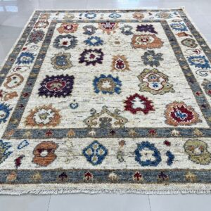 A cream rug with scattered colorful floral motifs and a gray border rests on white tile flooring.