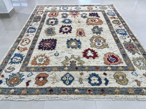 A cream rug with scattered colorful floral motifs and a gray border rests on white tile flooring.