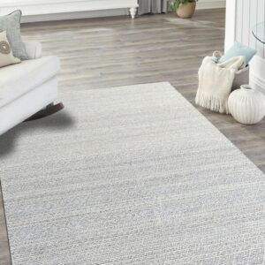 Light silver and white striated rug layered on gray wood floors in a bright, coastal room setting.